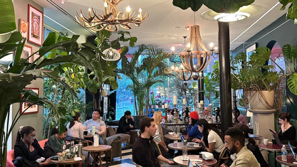 Cozy Cafe Flor in New York City featuring lush greenery, elegant chandeliers, and a vibrant atmosphere with people working and socializing.